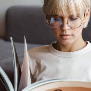 Ung kvinde med lyst hår og briller læser et magasin