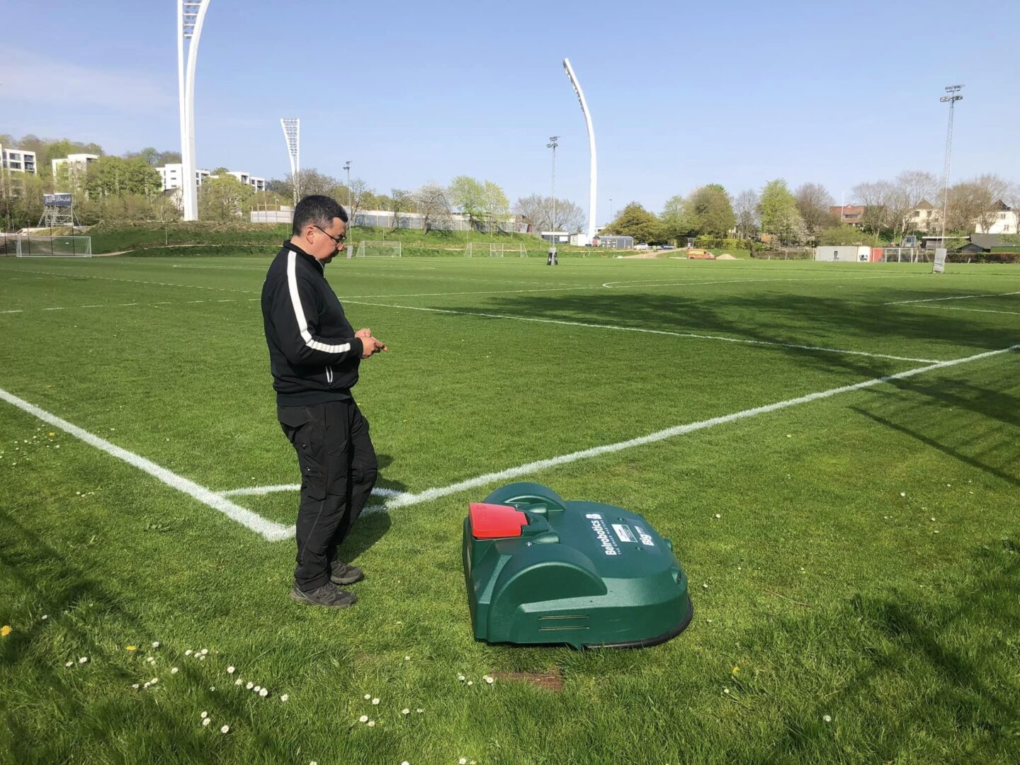 Billedet viser en mand og en robotplæneklipper på græsplæne